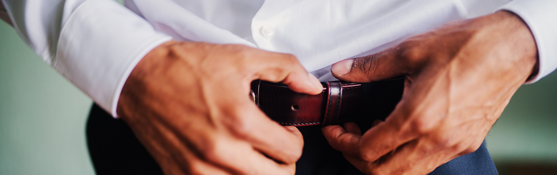 Close up of mans hands putting belt on his pants. Jak dobrać pasek do garnituru?